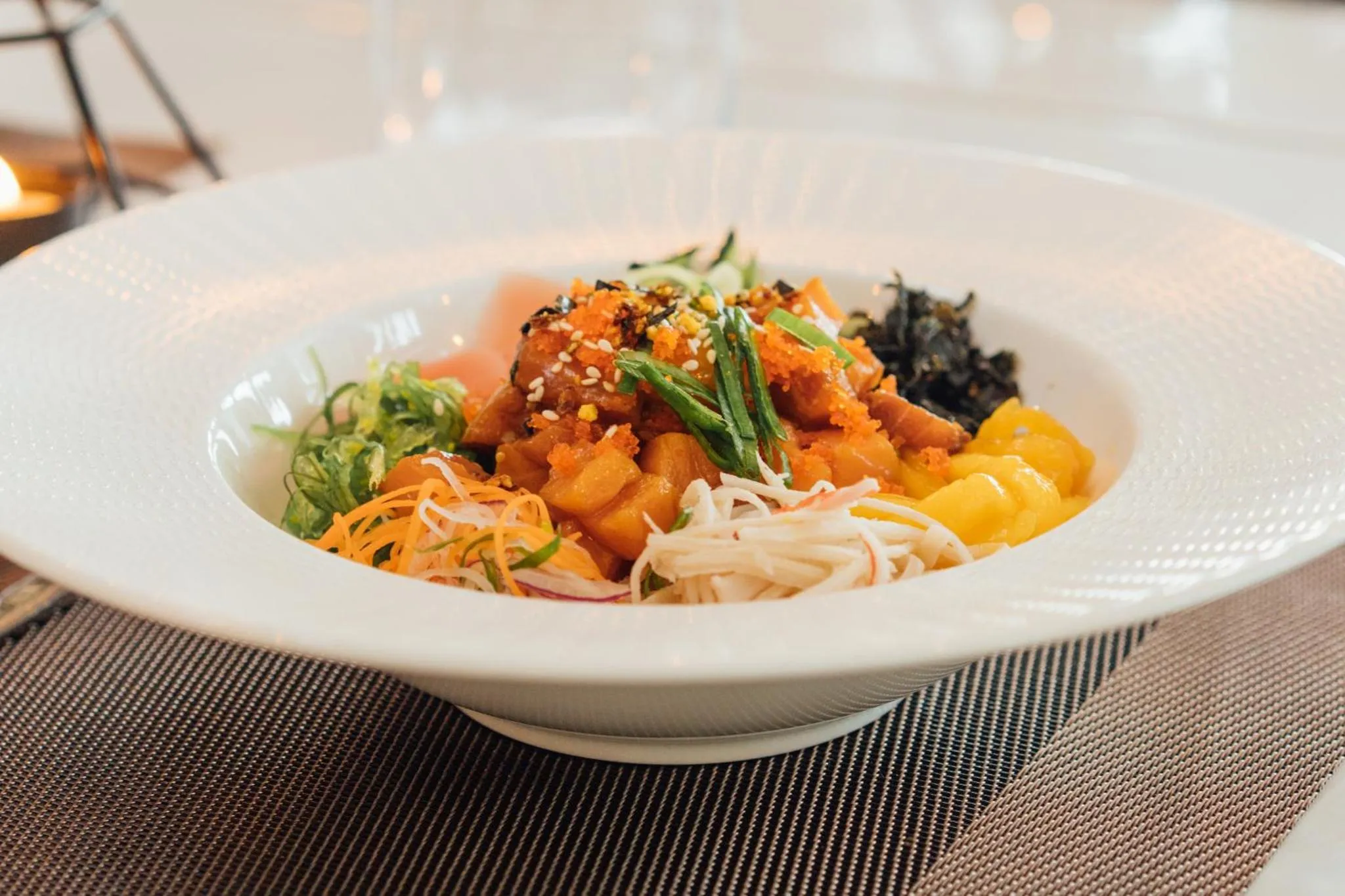 Un plat de poisson cru et de légumes colorés est présenté dans une assiette blanche.