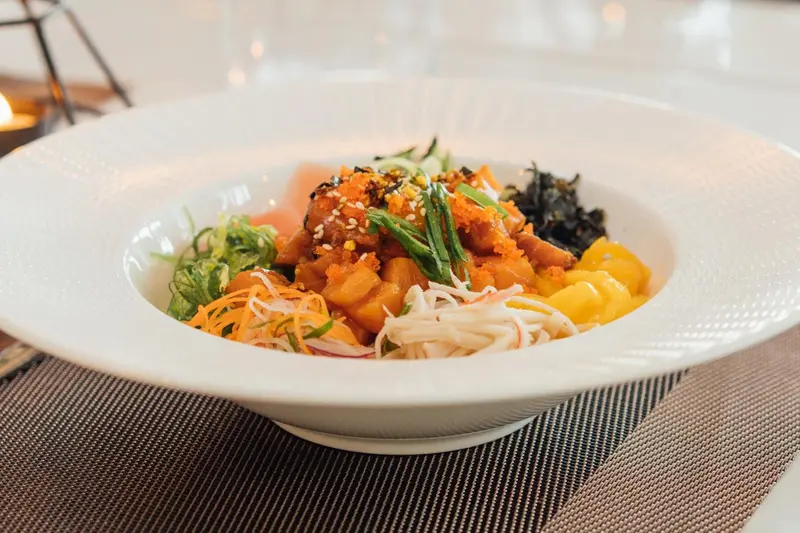 Un plat de poisson cru et de légumes colorés est présenté dans une assiette blanche.