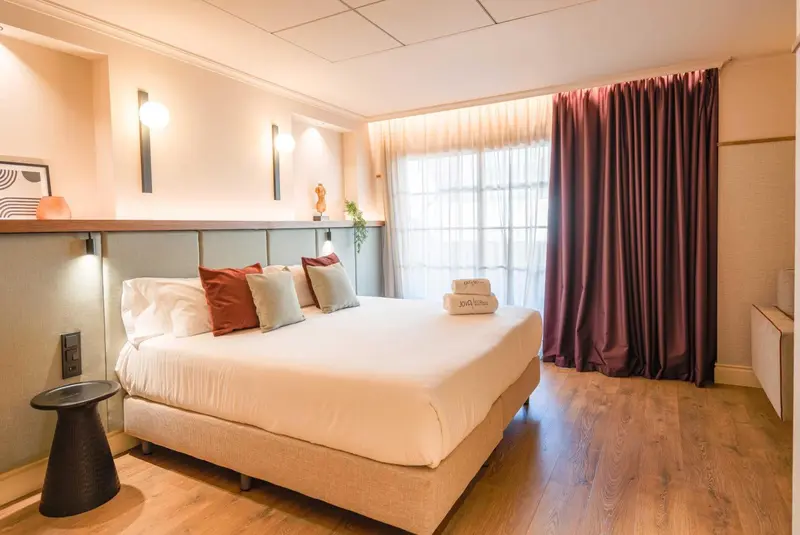 Une chambre lumineuse avec un grand lit recouvert d'une courtepointe blanche et de coussins colorés.