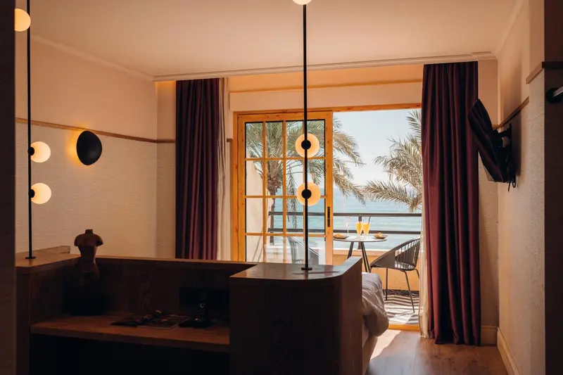 Une chambre d'hôtel lumineuse s'ouvre sur un balcon avec vue sur la mer.