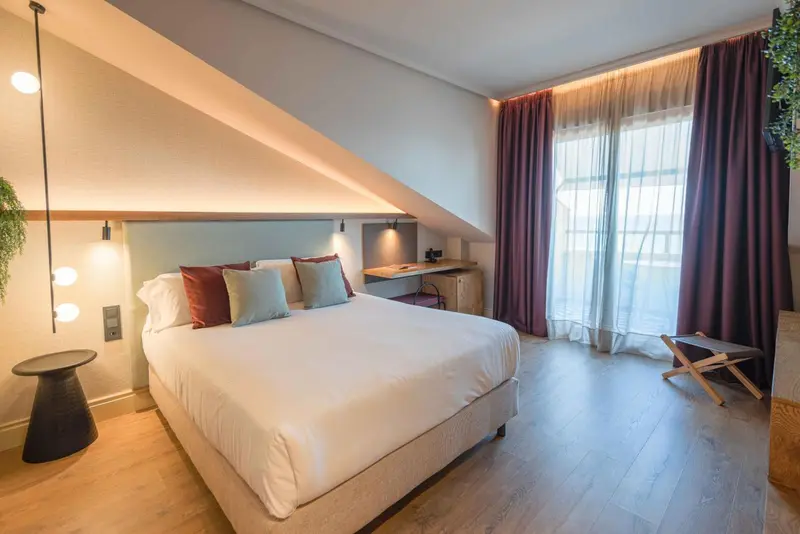Une chambre lumineuse avec un grand lit et des rideaux bordeaux.