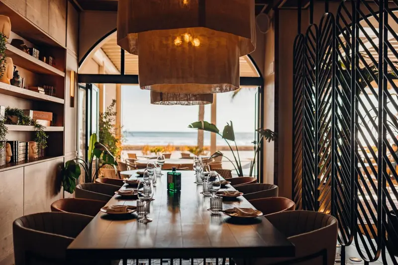 Une table de restaurant est dressée devant une grande baie vitrée donnant sur la mer.