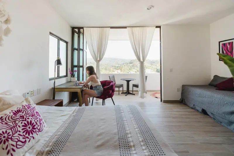 Une personne assise à un bureau dans une chambre lumineuse avec vue sur un paysage montagneux.