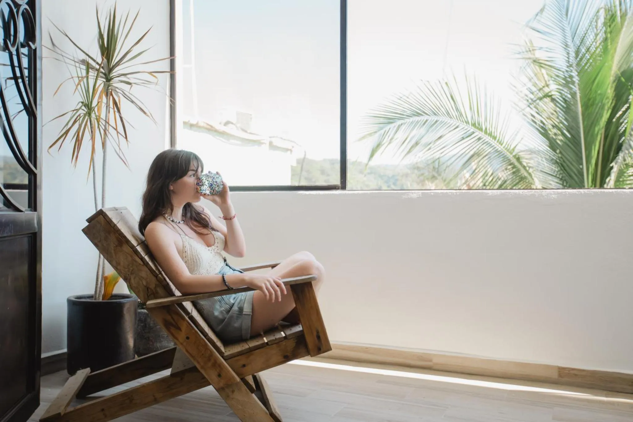 Une femme se détend sur une chaise en bois devant une grande fenêtre.