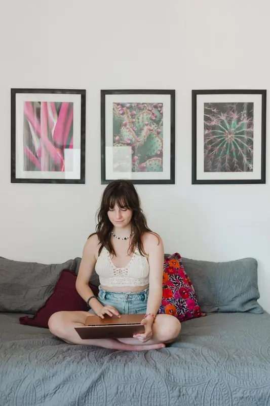 Une jeune femme est assise sur un lit devant un ordinateur portable.