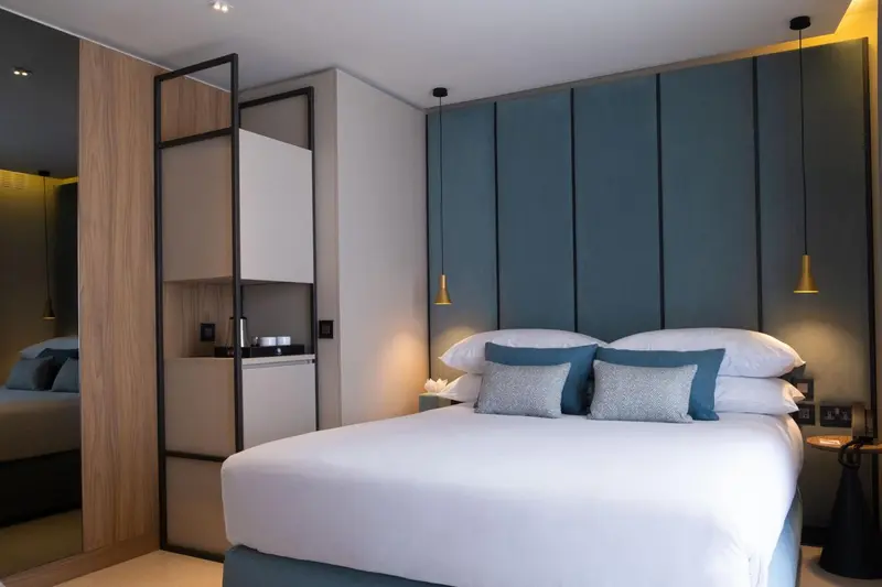 Une chambre moderne avec un grand lit recouvert de linge blanc et des coussins bleus.