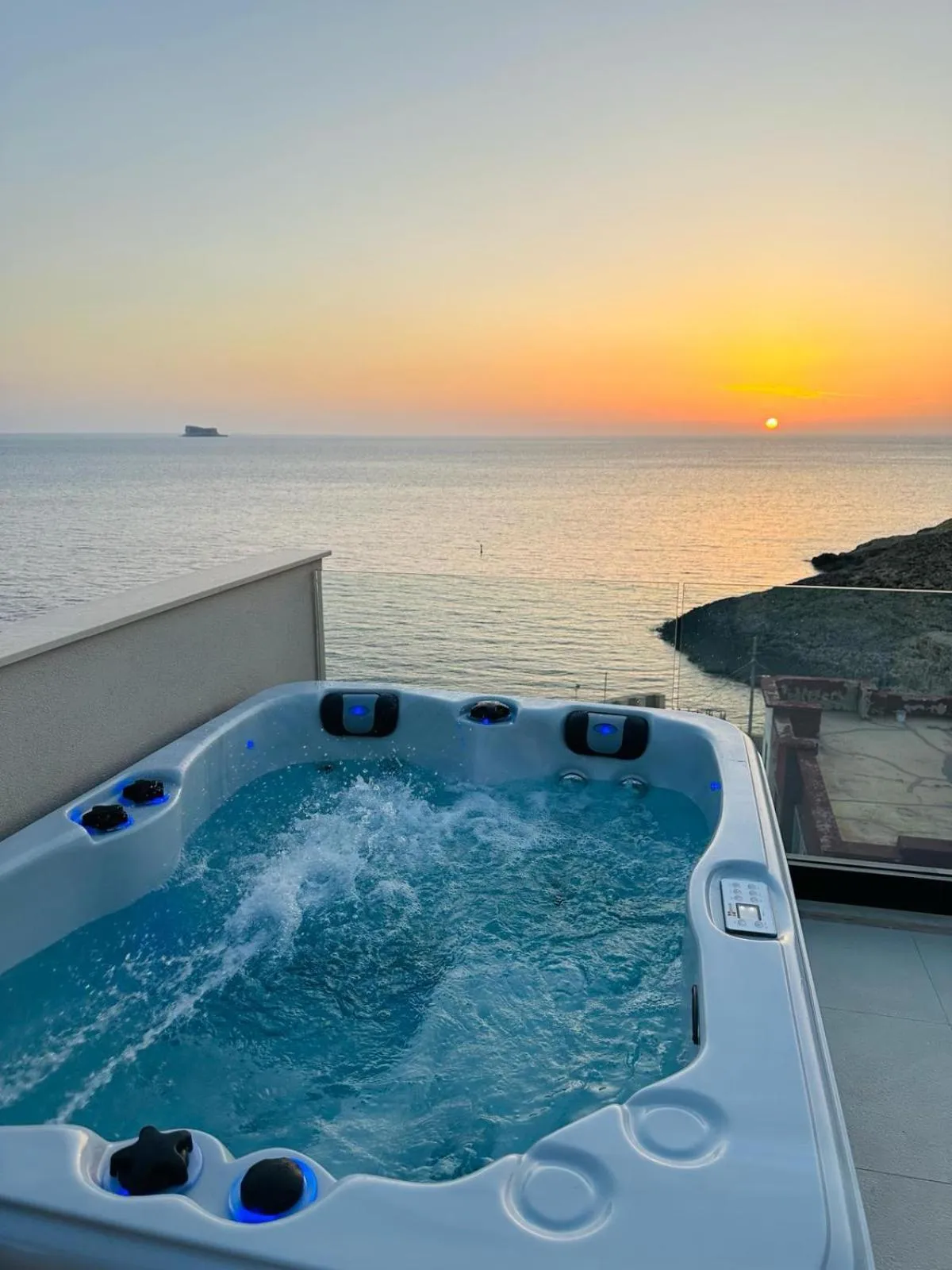 Un jacuzzi sur une terrasse avec vue sur la mer au coucher du soleil.
