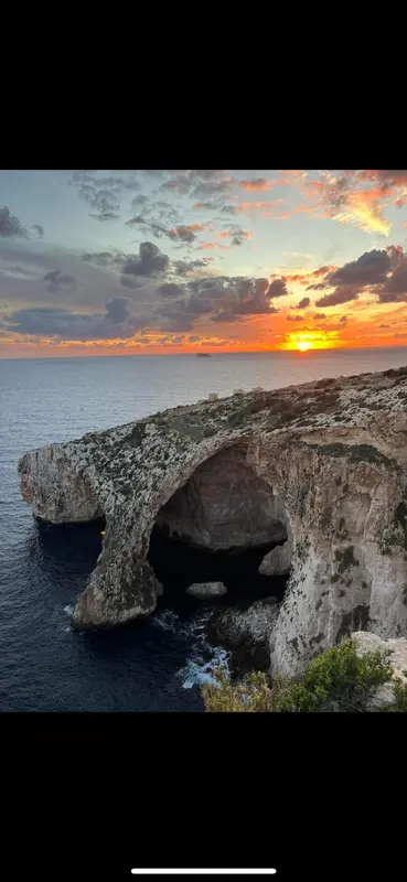 Coucher de soleil sur une côte rocheuse avec une arche naturelle.