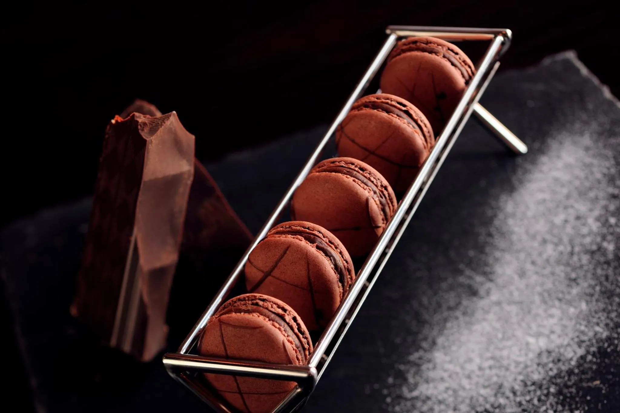 Présentation de macarons au chocolat sur un support métallique.