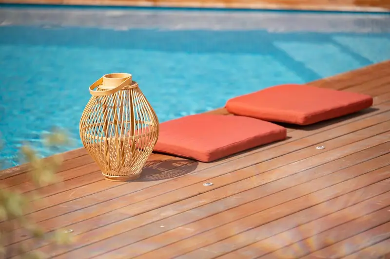 Une lanterne en osier repose sur une terrasse en bois près d'une piscine.