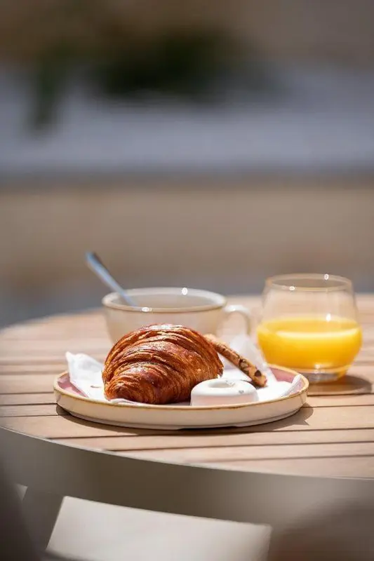 Une table en bois présente un croissant, une tasse et un verre de jus d'orange.