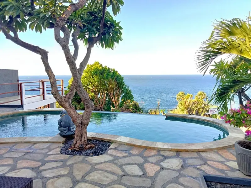 Une piscine à débordement surplombe la mer depuis une terrasse en pierre.