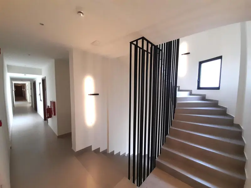 Un couloir d'hôtel mène à un escalier moderne avec des rampes en métal noir.