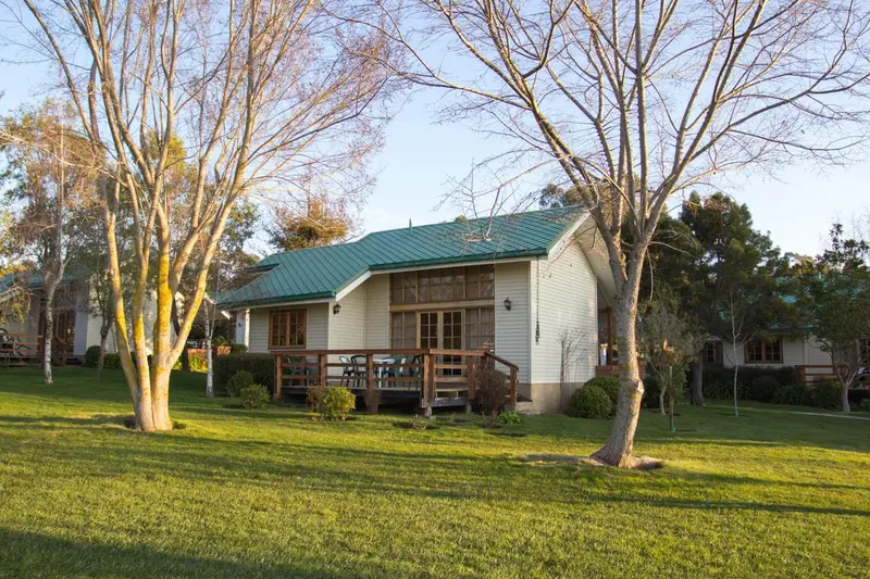 Bâtiment clair avec terrasse en bois au milieu d'une pelouse verte.