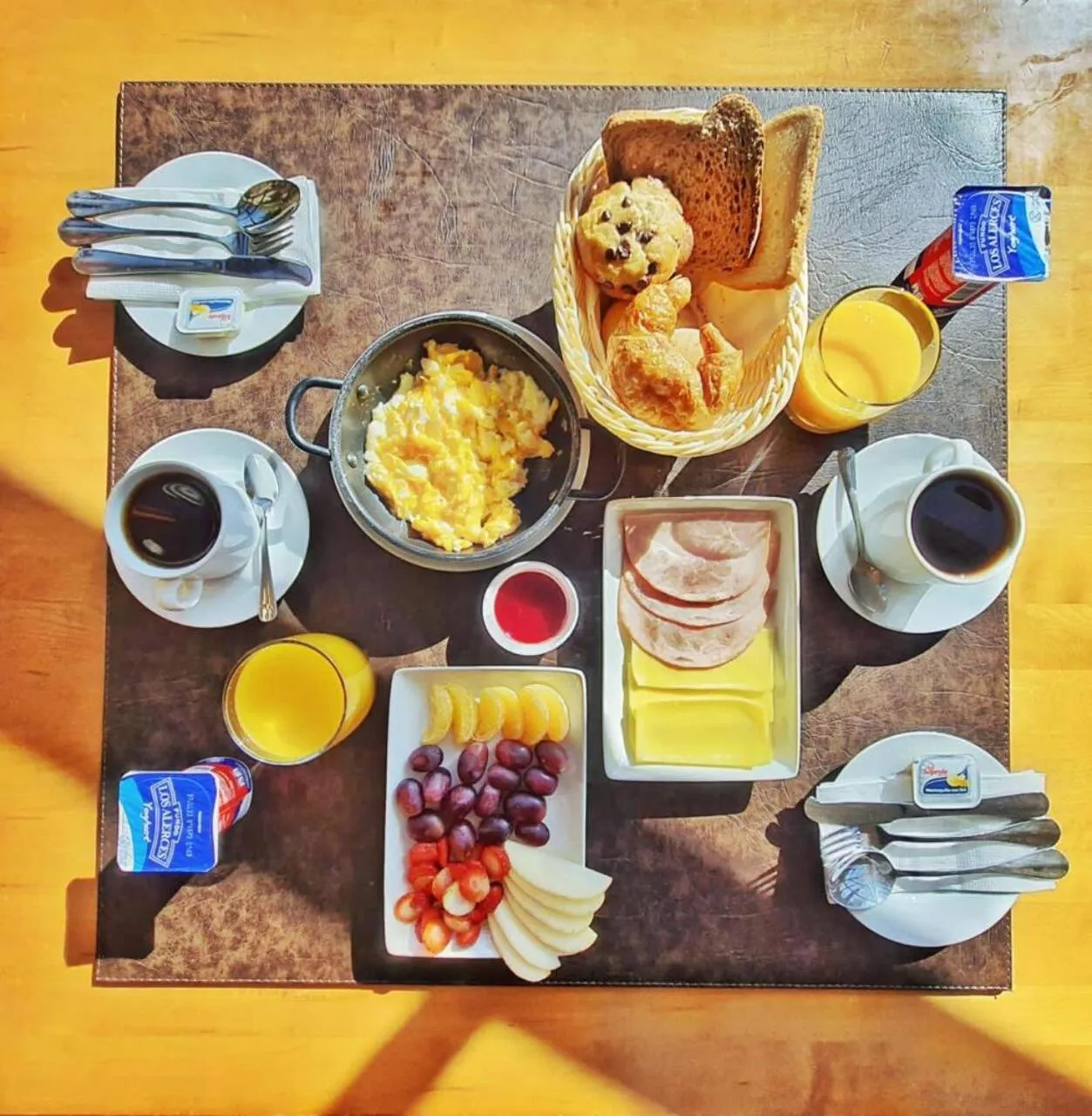 Table dressée avec un petit-déjeuner copieux composé de viennoiseries, d'œufs brouillés, de fruits et de boissons.