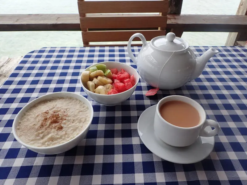 Une table avec un petit-déjeuner composé de fruits, de porridge et de thé.