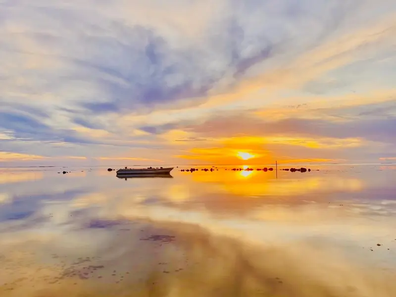 Coucher de soleil sur une mer calme avec un petit bateau à l'horizon.