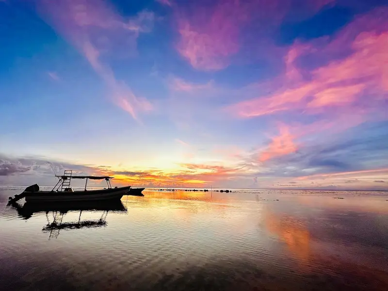 Coucher de soleil sur une mer calme avec des bateaux à l'horizon.