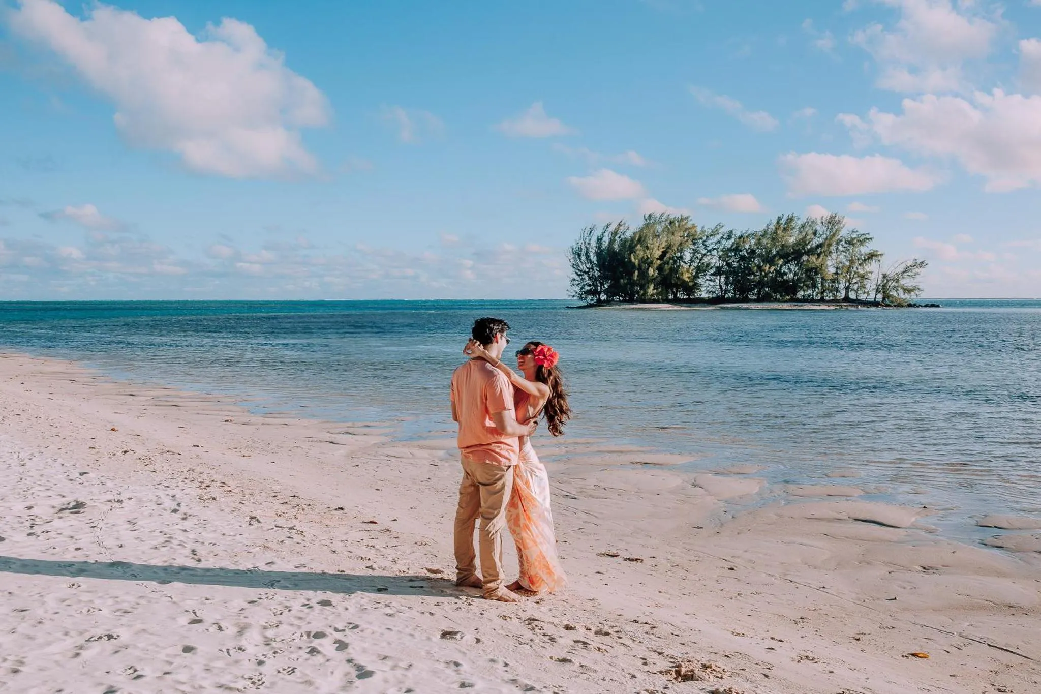 Un couple se tient sur une plage de sable blanc face à la mer.