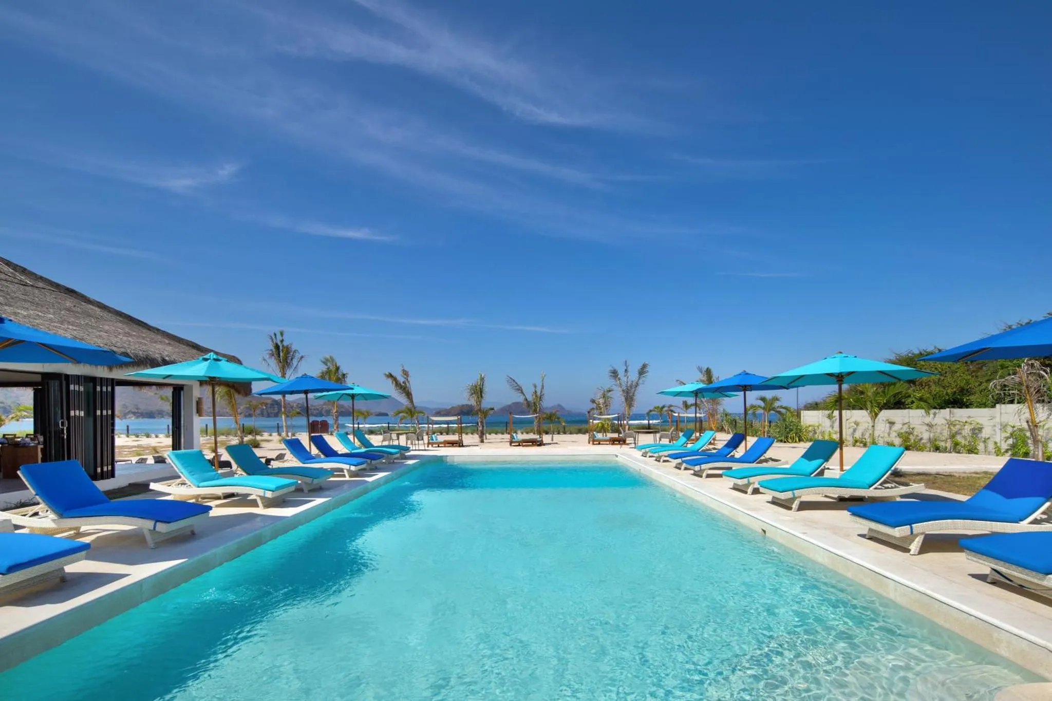 Transats bleus alignés au bord d'une piscine turquoise sous des parasols.