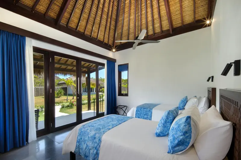 Chambre lumineuse avec lits jumeaux donnant sur un jardin tropical.