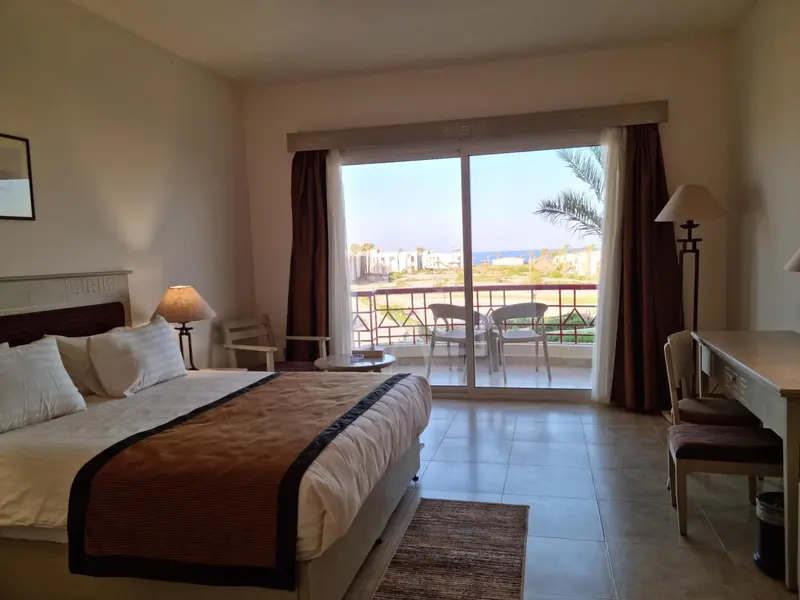 Chambre lumineuse avec un grand lit et une vue sur la mer depuis une terrasse.