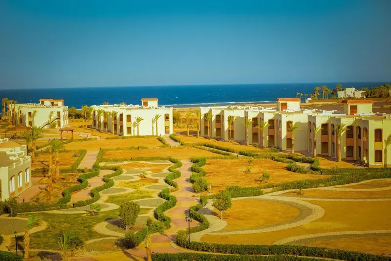 Vue aérienne d'un complexe hôtelier avec des bâtiments bas et des jardins soignés face à la mer.