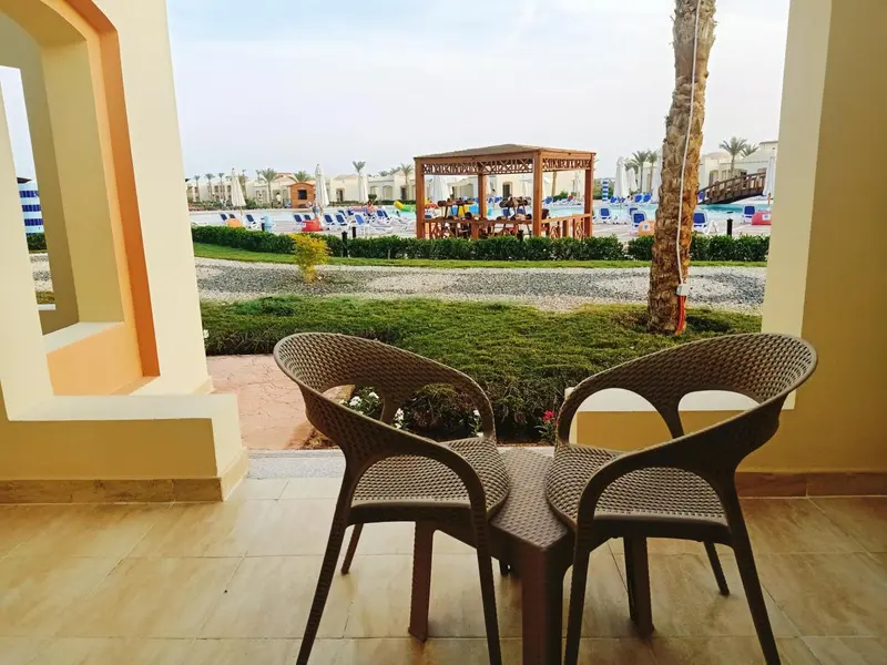 Deux fauteuils en plastique brun sur une terrasse carree, avec vue sur une piscine et des palmiers.