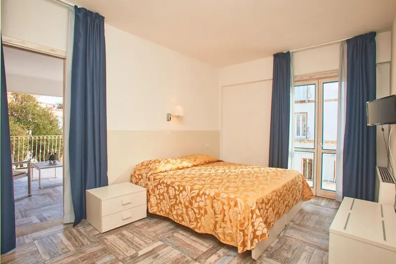Une chambre lumineuse avec un lit recouvert d'une couette à motifs et un accès à un balcon.