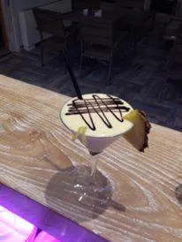 Un cocktail à la crème décoré de chocolat et d'une tranche d'ananas est servi sur un comptoir en bois.