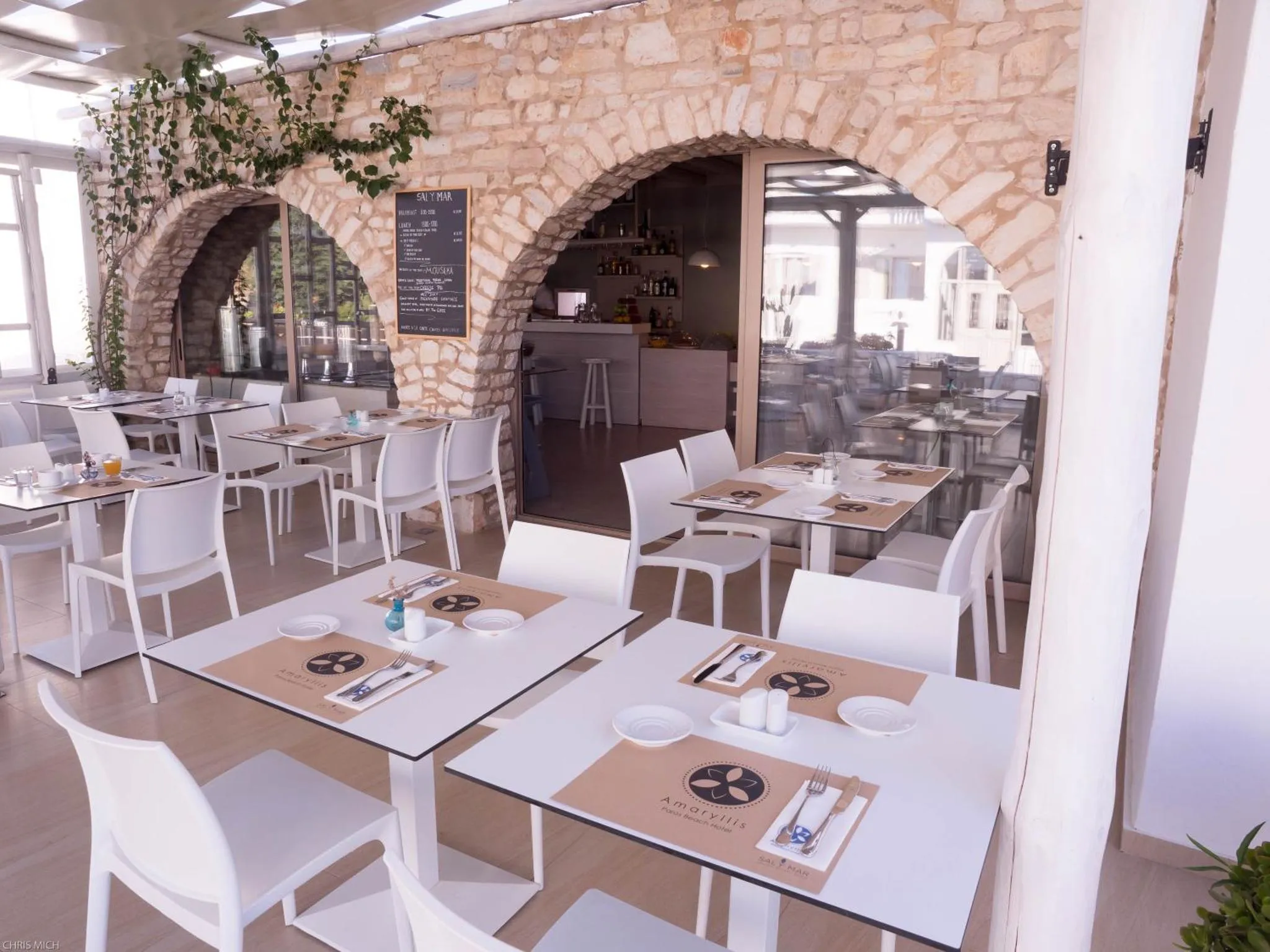 Terrasse ombragée avec tables et chaises blanches prêtes pour le service.