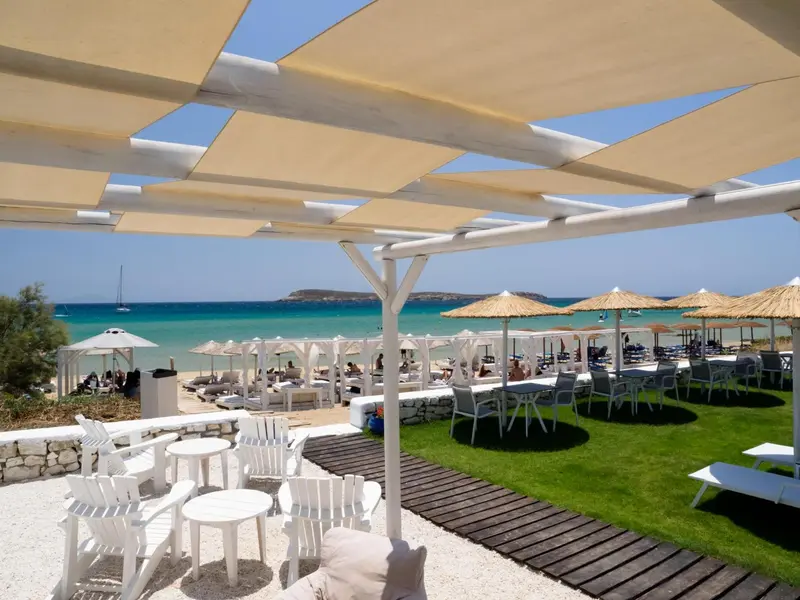 Terrasse ombragée avec vue sur une plage de sable fin et la mer.