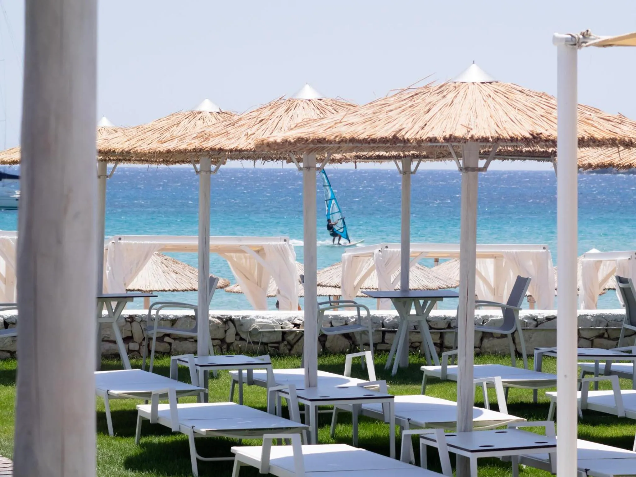 Terrasse ombragée avec tables et chaises face à la mer.