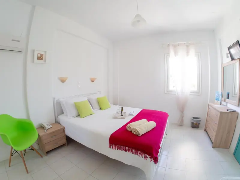 Une chambre lumineuse avec un lit recouvert d'une couverture rose et de coussins verts.