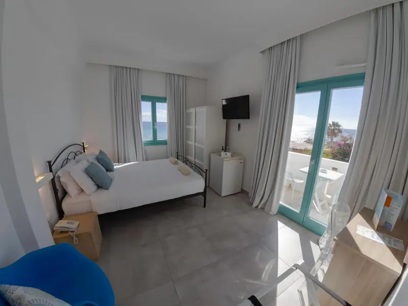 Chambre lumineuse avec un grand lit et vue sur la mer.