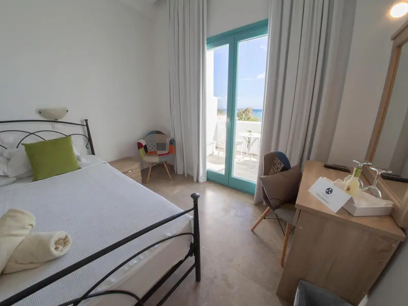 Chambre lumineuse avec un lit et un accès à une terrasse vue sur mer.