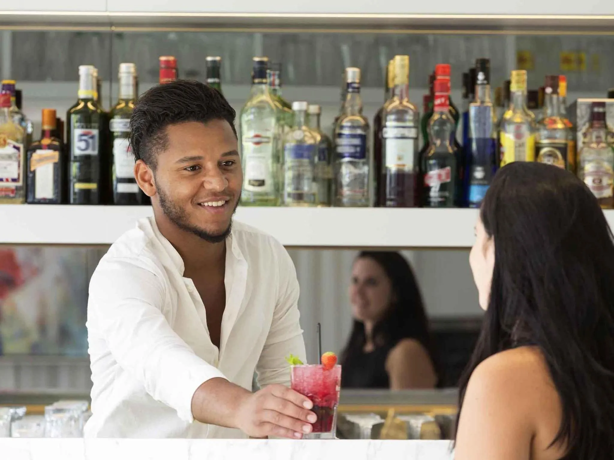 Un barman prépare une boisson pour une cliente.