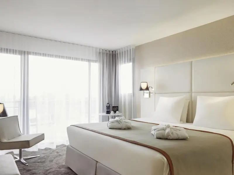 Une chambre lumineuse avec un grand lit et un fauteuil près d'une fenêtre.