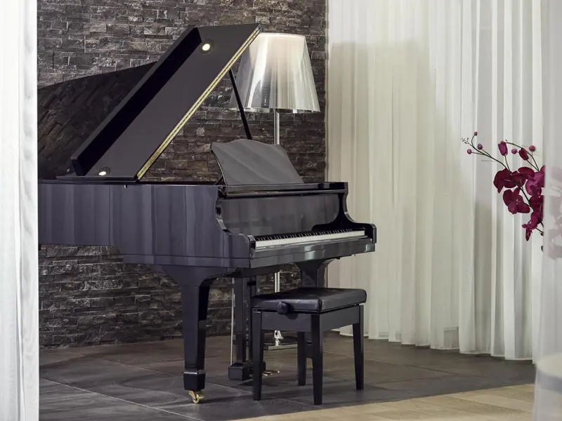 Un piano à queue noir se trouve devant un mur en pierre et des rideaux blancs.