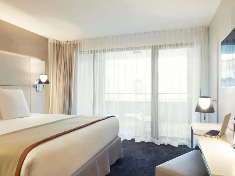 Une chambre lumineuse avec un grand lit et un bureau près d'une fenêtre.