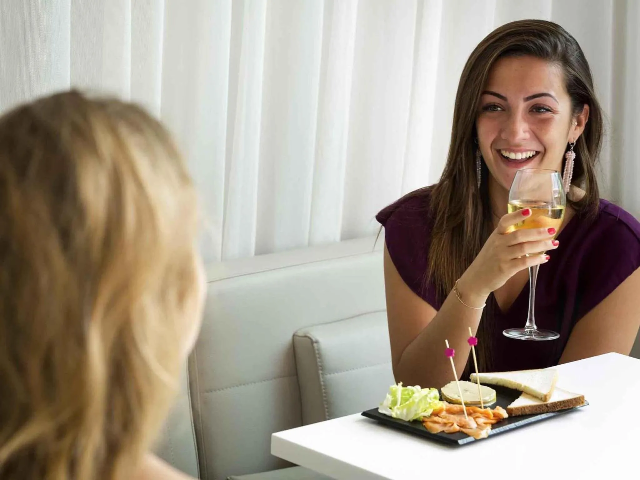 Une femme souriante tient un verre et une assiette de nourriture sur une table.