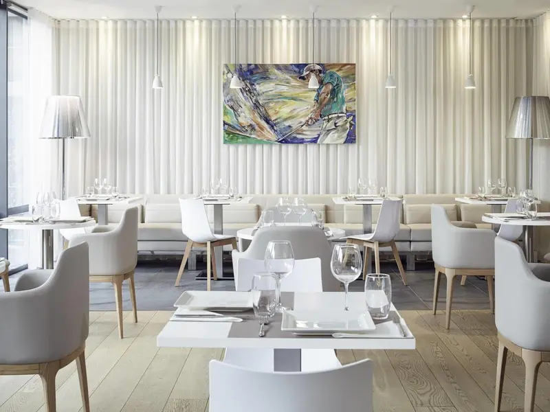 Une salle de restaurant lumineuse avec des tables dressées et des suspensions.