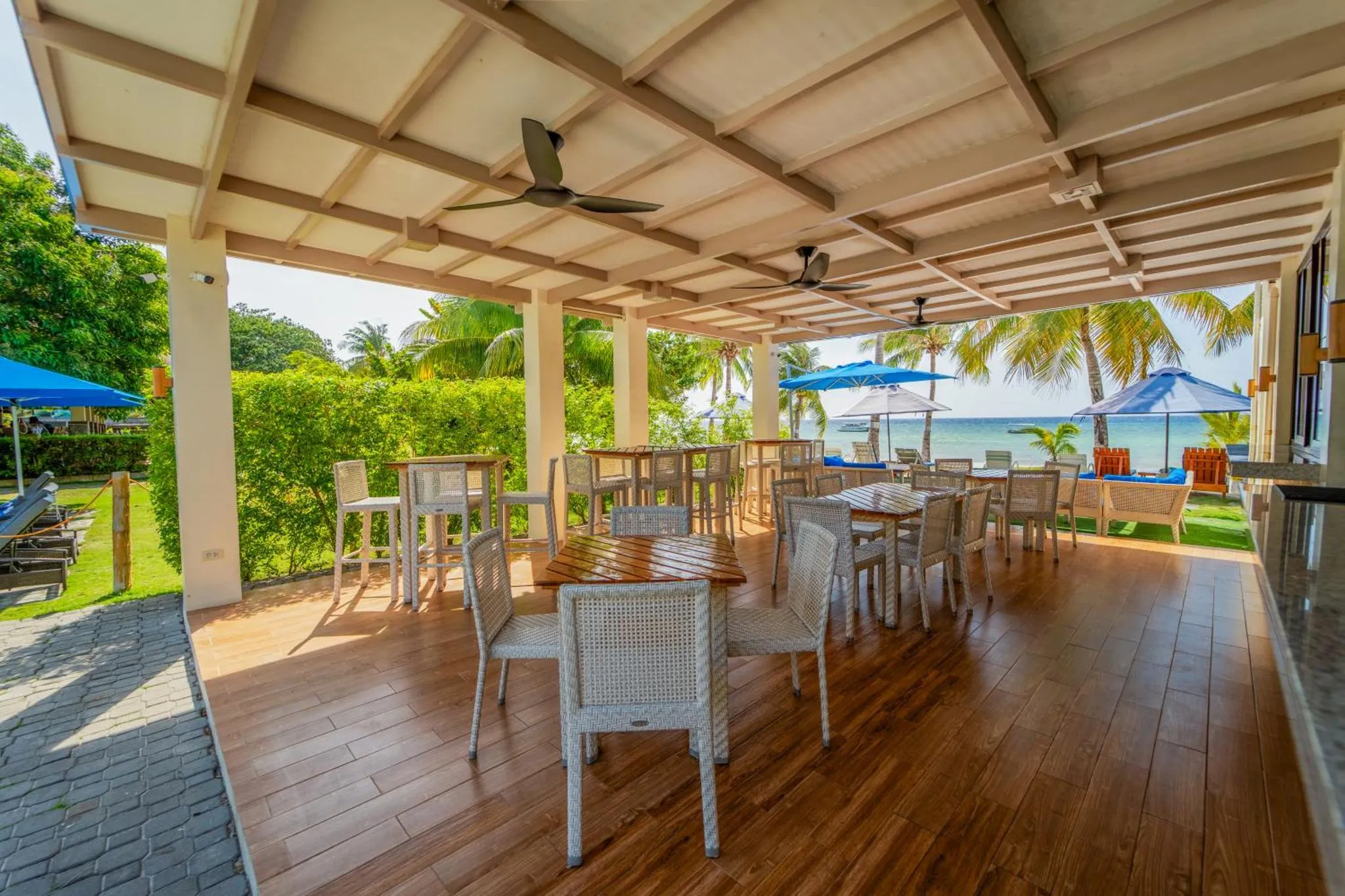 Terrasse ombragée avec tables et chaises en bois, vue sur la mer.