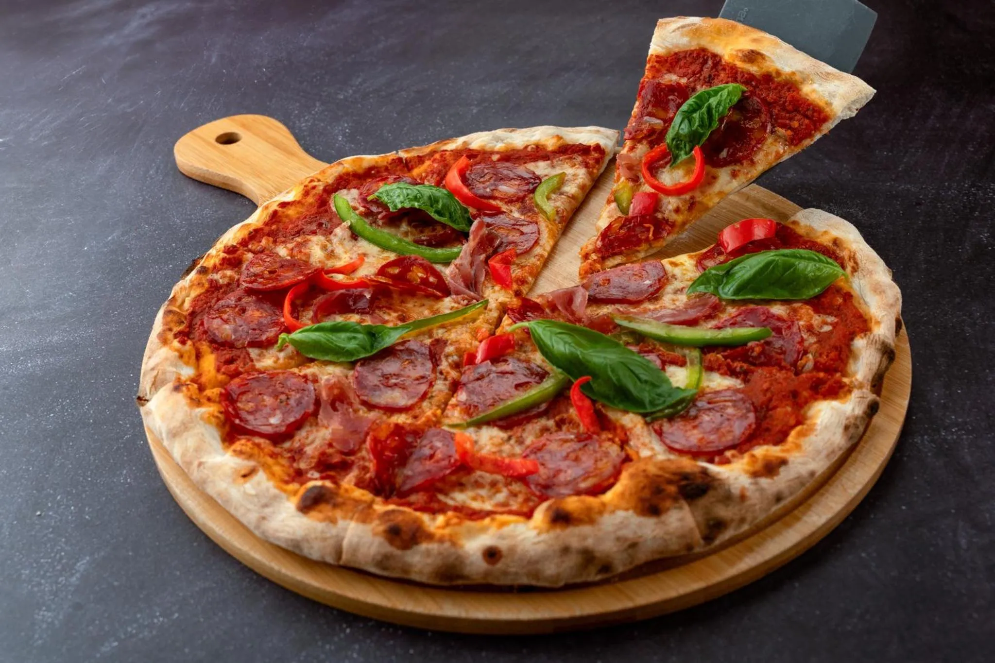 Une pizza entière est présentée sur une planche à découper en bois, avec une part retirée.