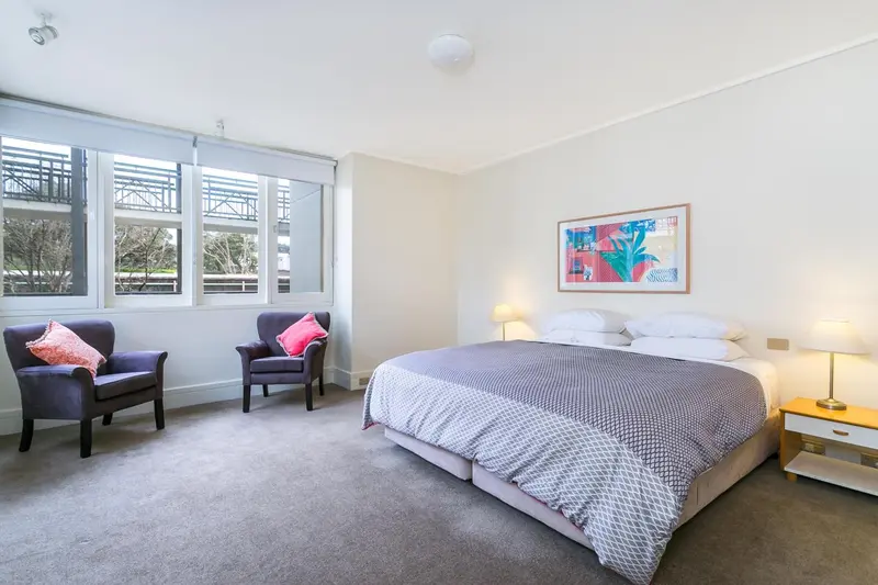 Une chambre lumineuse avec un lit double et deux fauteuils.