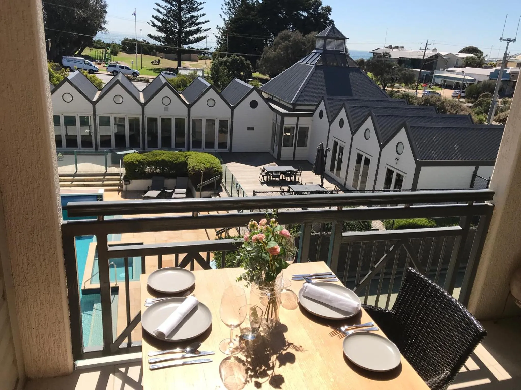 Une table est dressée sur une terrasse avec vue sur une piscine et des bâtiments.