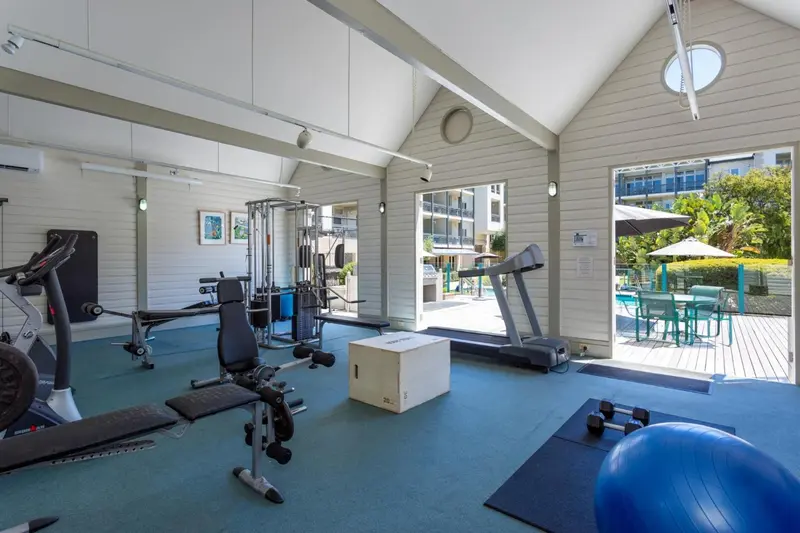 Une salle de sport lumineuse avec des équipements de musculation et un accès à une terrasse.