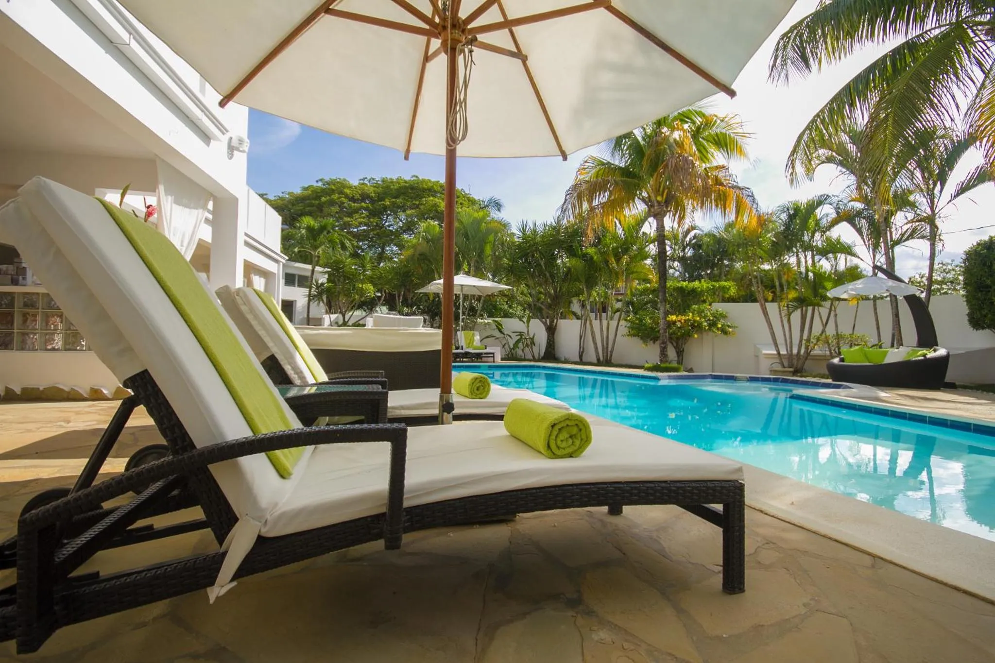 Transats et parasols bordent une piscine turquoise dans un cadre tropical.