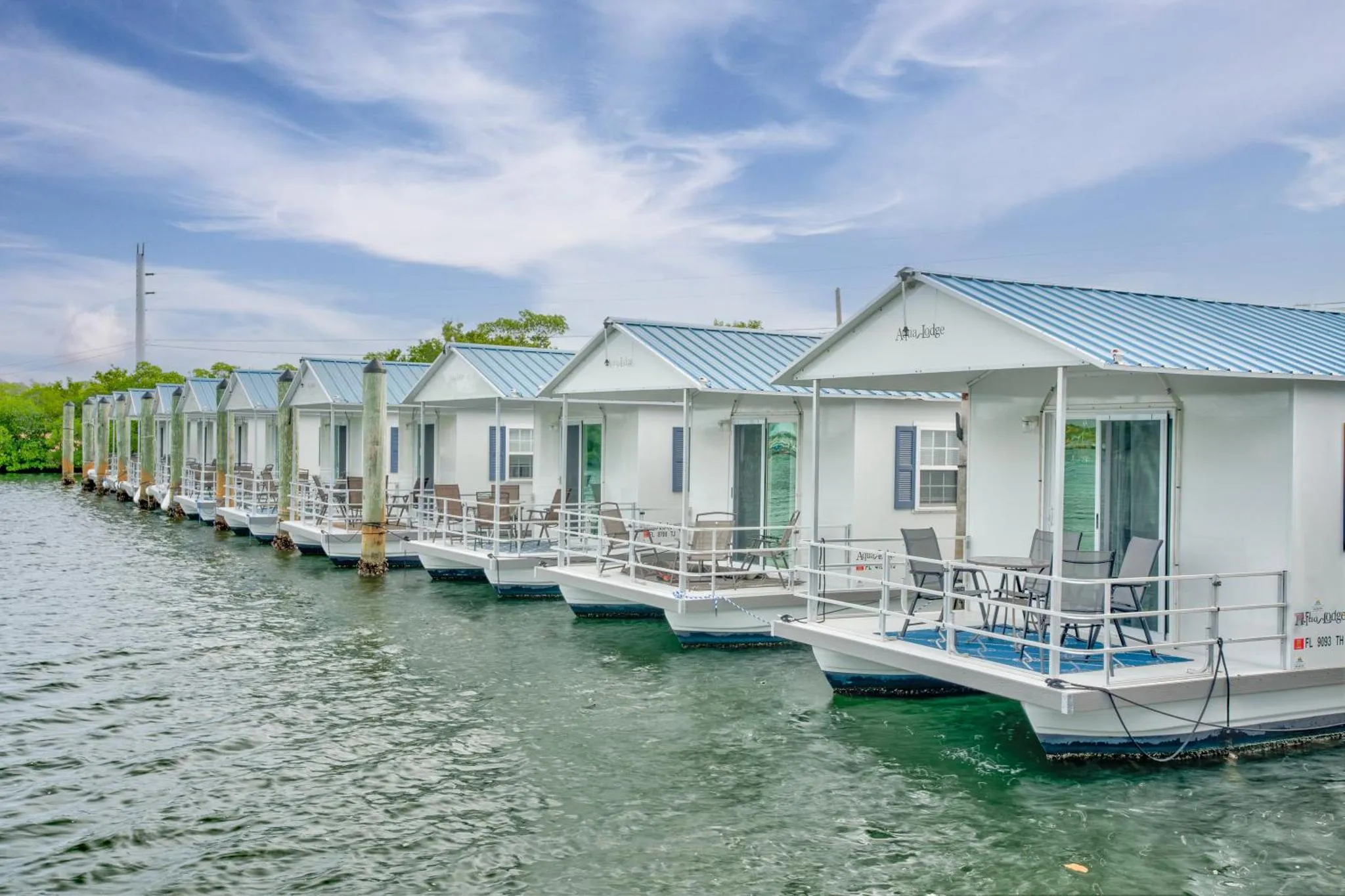 Cabanes flottantes blanches alignées sur l'eau turquoise sous un ciel nuageux.