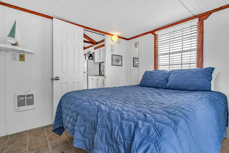 Une chambre lumineuse avec un lit recouvert d'une courtepointe bleue et une kitchenette.